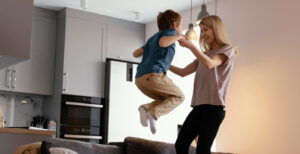 Un bambino piccolo in aria, sollevato giocando dalle mani di un adulto in una cucina moderna, con il bambino che sembra tendere verso una lampada a sospensione.